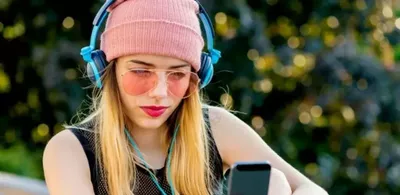 En dame med rosa lue, solbriller og headset ser på telefonen sin. Foto